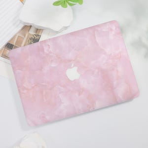 May include: A pink marble-patterned laptop case with a white Apple logo. The case has a smooth, glossy finish and a light pink color with darker pink and white veining. The laptop case is a protective accessory for a computer.
