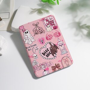 May include: Pink Halloween-themed case with various spooky illustrations. Features ghosts, pumpkins, bats, and the text "Dead Inside But Cute" and "Bite Me". The case has a decorative bow and a tombstone design.