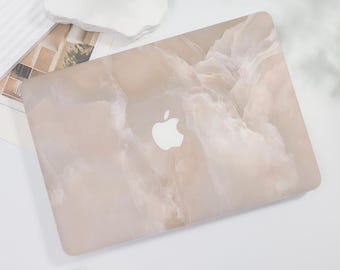 May include: A laptop skin with a beige marble pattern and a white Apple logo. The skin is designed to protect the laptop from scratches and wear.