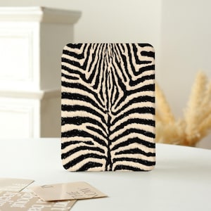 May include: A rectangular electronic reader cover featuring a high-contrast black and cream zebra stripe pattern. The design displays a symmetrical arrangement of organic, flowing lines that mimic the natural fur texture of a zebra across the surface.