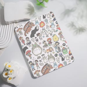 May include: White tablet case with a colorful cartoon print of characters from the animated film 'My Neighbor Totoro'. The characters include Totoro, Catbus, and other characters from the film.