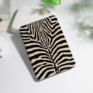 May include: A rectangular case with a zebra print design. The case features a pattern of black stripes on a cream-colored background, creating a striking contrast. The case is likely for a tablet or e-reader.
