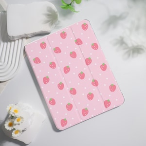 Könnte beinhalten: Rosa Tablet-Hülle mit einem sich wiederholenden Muster aus roten Erdbeeren und weißen Punkten. Die Hülle ist aufgeklappt und gibt den Blick ins Innere frei. Die Erdbeeren haben grüne Blätter. Die Hülle liegt auf einer weißen Oberfläche.