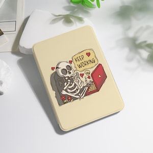 May include: A beige tablet case featuring a cartoon skeleton working on a red laptop. The skeleton is sitting on a tombstone with the letter "R" and the words "KEEP WORKING" in a speech bubble. Red hearts and flowers are also present.