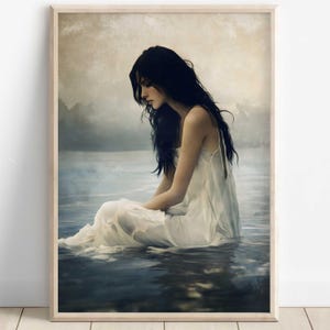 Puede incluir: Una impresión artística enmarcada representa a una persona con cabello largo y oscuro sentada en el agua, vestida con un vestido blanco. La obra de arte tiene una calidad suave y etérea, con tonos apagados de azul, gris y blanco. La persona mira hacia abajo.