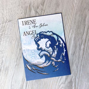 Puede incluir: Invitación de boda azul con un fondo de acuarela blanca y un diseño de ola recortada. La invitación dice "Irene & Ann Gelinas Angel & Carlos Mendes".