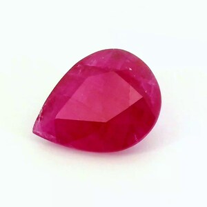 Puede incluir: Una gema de rubí facetada en forma de pera. La gema es de un color rojo intenso y vibrante con múltiples facetas que reflejan la luz. La piedra está sobre un fondo blanco.