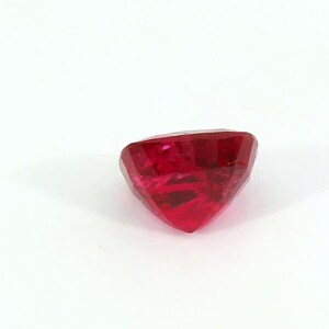 May include: A faceted, heart-shaped, deep red gemstone. The gem is cut with multiple facets, creating a sparkling effect. The stone is set against a plain white background, highlighting its color and shape. This gemstone is suitable for jewelry making.
