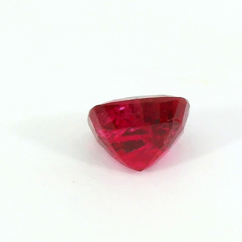 May include: A faceted, heart-shaped, deep red gemstone. The gem is cut with multiple facets, creating a sparkling effect. The stone is set against a plain white background, highlighting its color and shape. This gemstone is suitable for jewelry making.