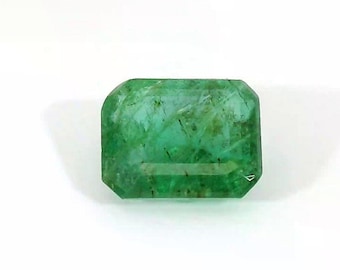 May include: A rectangular emerald gemstone with a vibrant green hue. The gem has a faceted cut with beveled edges, reflecting light. The stone is set against a white background, highlighting its clarity and color.