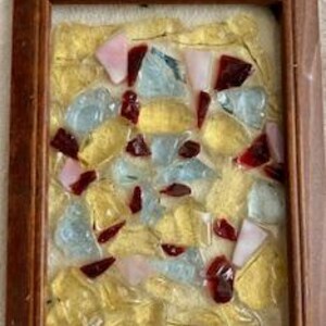 以下が含まれることがあります： 黄色、赤、ピンク、青の色合いのガラス片を様々な形で組み合わせたモザイクアートが額装されています。ガラス片はランダムなパターンで配置され、ユニークで抽象的なデザインを生み出しています。