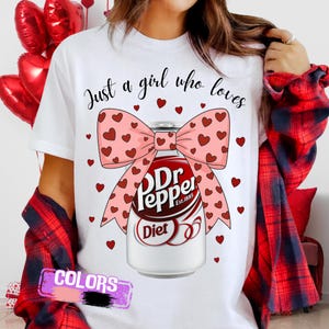 May include: White t-shirt with the text "Just a girl who loves" above a Dr. Pepper Diet can design. The can is adorned with a pink bow covered in red hearts. Small red hearts are scattered around the design.