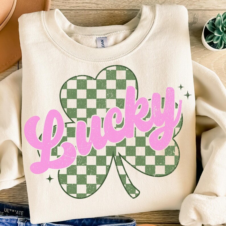 May include: A cream-colored sweatshirt with a green and white checkered shamrock and the word "Lucky" in pink lettering.