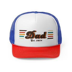 May include: A trucker hat with a white front panel, a red brim, and a blue mesh back. The hat features the word "Dad" in a retro font, with the text "Est. 2024" below it. The design includes horizontal stripes in various colors.