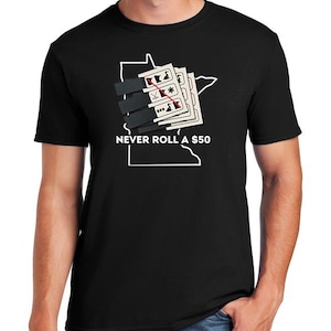 Puede incluir: Camiseta negra con el texto blanco "NEVER ROLL A $50". El diseño incluye un contorno blanco de un estado, con naipes y un símbolo de dinero.