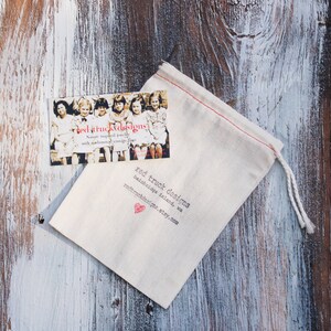 May include: A small, off-white drawstring bag and a business card rest on a weathered wooden surface. The card features a vintage photo and the text "red truck designs." The bag has red stitching and the brand name printed on it.