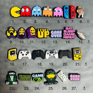 May include: A set of 27 colourful shoe charms featuring video game characters and themes. The charms include Pac-Man, a skeleton, a level up sign, a game over sign, a controller, and a Halo character.