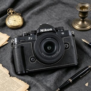 May include: A black Nikon Zf mirrorless camera with a textured leather-like grip and white stitching. The camera features a prominent lens, a viewfinder housing with the Nikon logo, and various manual control dials on the top plate.