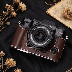 May include: A black Fujifilm X-T50 digital camera with a brown leather-textured half case featuring white contrast stitching. The camera is equipped with a Fujinon Aspherical Lens Super EBC XC 15-45mm 1:3.5-5.6 OIS PZ lens with a 52mm filter diameter.