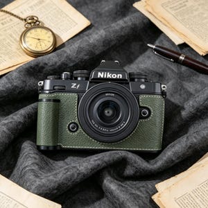 May include: A black Nikon Zf mirrorless camera featuring a textured olive green leather-like grip with white contrast stitching. The camera body displays the Nikon logo and Zf model name, equipped with a black lens and various manual control dials.