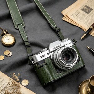 May include: A silver Fujifilm X-T30 camera encased in a textured dark green leather half-case with a matching green leather camera strap featuring white stitching. The camera body is silver with black accents and a lens attached to the front.