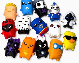 May include: A collection of fourteen small, stylized character figurines featuring diverse designs, including a yellow duck with sunglasses, a blue superhero figure, a white ghost, a black skull-themed character, and various colorful creatures.
