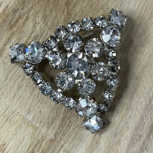 May include: A silver tone brooch with a cluster of clear rhinestones in a triangular shape.