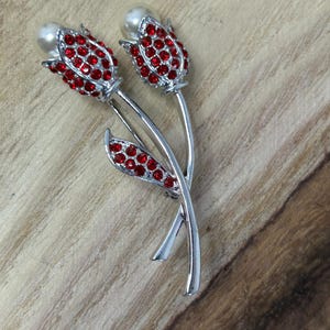 May include: A silver brooch with two red jeweled tulips with pearl centers.