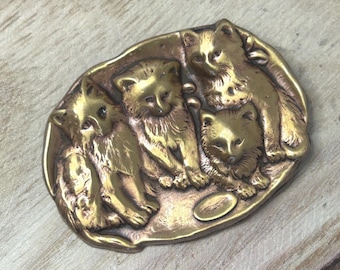 May include: A vintage brass oval-shaped belt buckle featuring a relief sculpture of four kittens. The kittens are clustered together, with detailed fur and facial features. The buckle has a warm, antique gold tone.