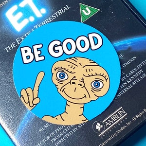 May include: A blue and white round sticker with the words "Be Good" and an image of E.T. the Extra-Terrestrial from the movie E.T. The Extra-Terrestrial.