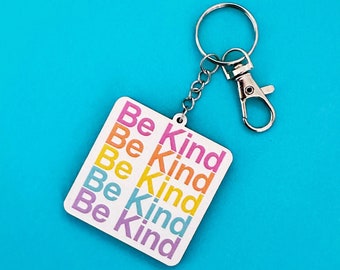May include: White keyring with a square tag that says "Be Kind" five times in different colours. The keyring is attached to a silver metal ring and a silver metal clasp.