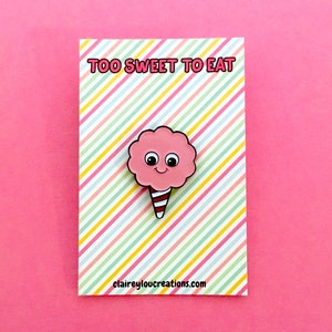 May include: Pink cotton candy enamel pin with a smiling face and red and white striped stick. The pin is on a card with the text "Too Sweet To Eat" and the website "claireyloucreations.com".
