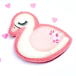 May include: A pink felt swan with a white belly and a pink flower made of sequins on its chest.