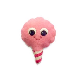 May include: A pink cotton candy plush toy with a smiling face and googly eyes. The cotton candy is on a stick with pink and white stripes.
