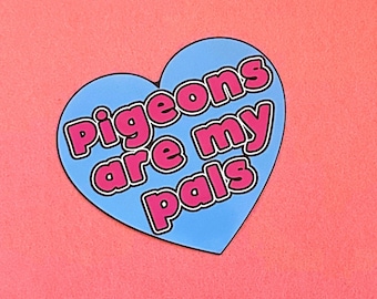 May include: A heart-shaped sticker with the phrase "Pigeons are my pals" in pink text with a white outline, set against a light blue background. The sticker is on a pink background.