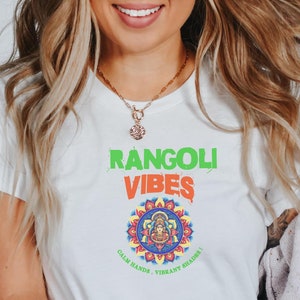 May include: White t-shirt with a green and orange graphic that says "Rangoli Vibes" and features a colourful mandala with the text "Calm Hands, Vibrant Souls".