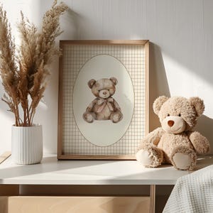 May include: A framed print of a watercolor illustration of a brown teddy bear wearing a pink bow, set against a white background with a brown and white checkered border. A plush brown teddy bear sits on a white surface in front of the print.