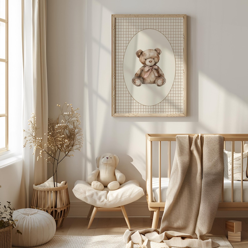 May include: A brown teddy bear with a pink bow sits in an oval frame with a beige background and a brown and white checkered border. The frame is hanging on a white wall in a nursery.
