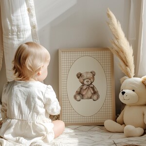 May include: A framed watercolor illustration of a brown teddy bear with a pink bow sitting in a beige oval on a white and brown checkered background. The frame is made of light wood.