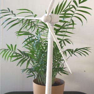 Könnte beinhalten: Ein weißes Modell einer Windkraftanlage mit drei Rotorblättern, das auf einem Holztisch neben einer Topfpflanze steht.