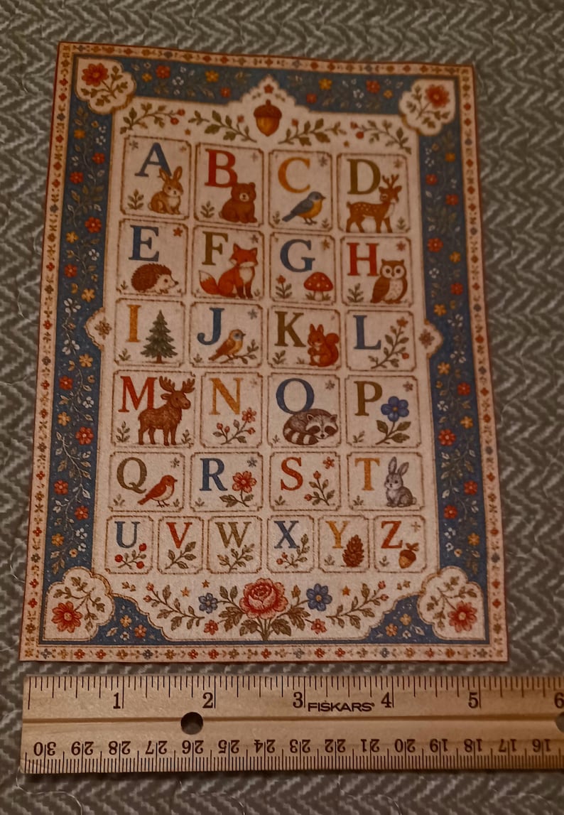May include: A rectangular alphabet print featuring letters A through Z, each paired with a nature-themed illustration like animals, plants, and mushrooms. A wooden Fiskars ruler is placed below, showing the print is approximately 5.5 inches wide.