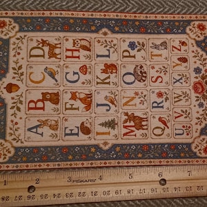 May include: A rectangular alphabet card featuring colorful letters A through Z paired with woodland animal and nature illustrations, bordered by a floral pattern. A wooden ruler placed below shows the card is approximately 8 inches wide.