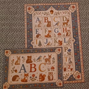 May include: Two rectangular prints featuring an alphabet theme with woodland animals and botanical motifs. The designs include letters A through Z, illustrated with creatures like bears, foxes, owls, and deer, framed by a blue floral border.