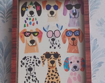 May include: A framed artwork featuring nine cartoon dogs, each with unique patterns and sunglasses. The dogs are in various colors, including orange, pink, and black, set against a white background. The frame is a dark brown color.