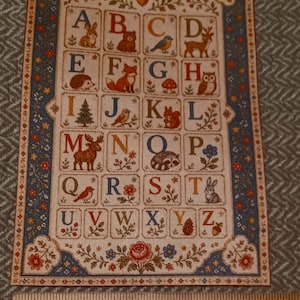 May include: A rectangular alphabet print featuring letters A through Z, each paired with a nature-themed illustration like animals, plants, and mushrooms. A wooden Fiskars ruler is placed below, showing the print is approximately 5.5 inches wide.