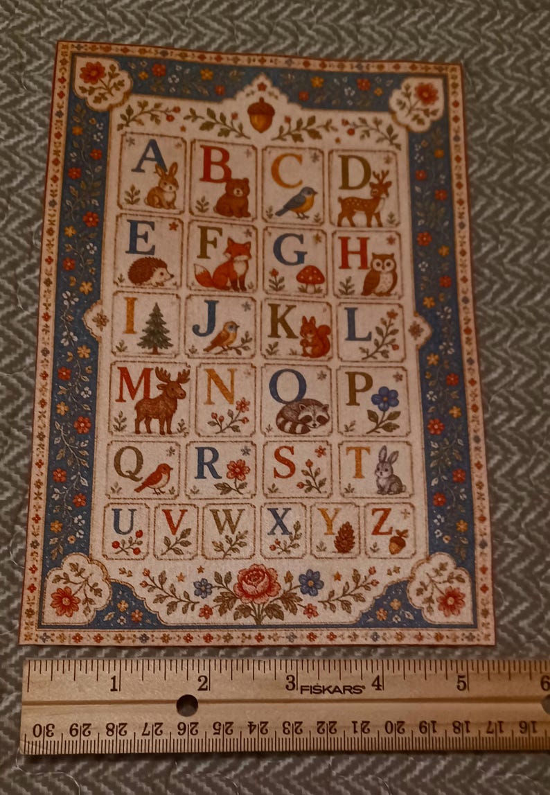 May include: A rectangular alphabet print featuring letters A through Z, each paired with a nature-themed illustration like animals, plants, and mushrooms. A wooden Fiskars ruler is placed below, showing the print is approximately 5.5 inches wide.