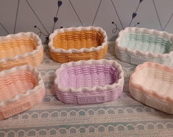 May include: Six small, pastel-colored ceramic baskets with a woven texture and scalloped edges. The baskets are in shades of yellow, orange, pink, purple, and blue. The word "baby" is embossed on some of the baskets.