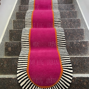 Könnte beinhalten: Ein Treppenläufer-Teppich mit einem leuchtenden fuchsiafarbenen Mittelteil, umrandet von einem orangefarbenen Rand und schwarz-weiß gestreiften Kanten. Der Teppich liegt auf einer Granittreppe. Die Worte "URBAN HOME RUG" sind auf dem Teppich aufgedruckt.
