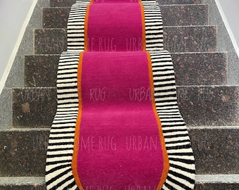 Könnte beinhalten: Ein Treppenläufer-Teppich mit einem leuchtenden fuchsiafarbenen Mittelteil, umrandet von einem orangefarbenen Rand und schwarz-weiß gestreiften Kanten. Der Teppich liegt auf einer Granittreppe. Die Worte "URBAN HOME RUG" sind auf dem Teppich aufgedruckt.