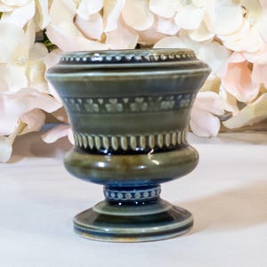 May include: A small, green and blue ceramic urn with a pedestal base. The urn has a decorative design of shamrocks and a scalloped rim.